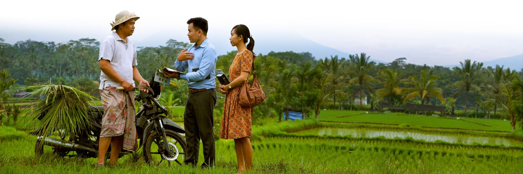 Two of Jehovah's Witnesses preaching to a man in a rice paddy.