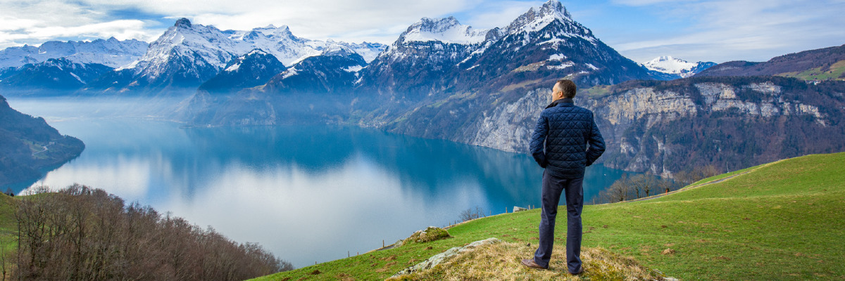 A man looks at the reflection of snow-capped mountains on a lake