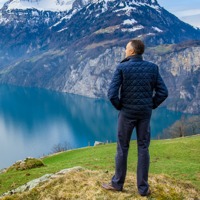 A man looks at the reflection of snow-capped mountains on a lake