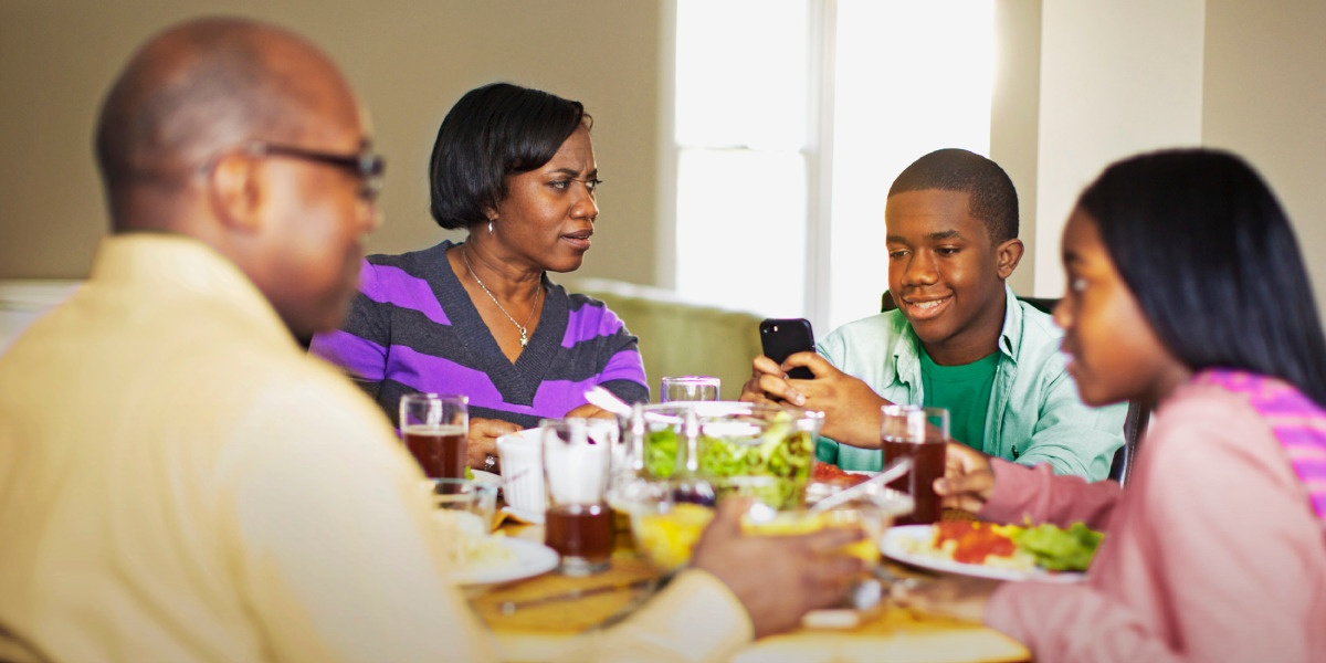 Un joven texteando mientras el resto de la familia come