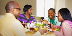 ایک نوجوان اپنے گھر والوں کے ساتھ کھانا کھاتے وقت فون پر میسج کر رہا ہے۔‏