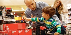 A little boy is reaching for a toy on a store shelf and his father is saying no