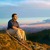 Un uomo seduto sulla vetta di una montagna osserva il paesaggio e il cielo suggestivo