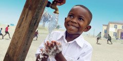 A young boy washes his hands at an outdoor spigot