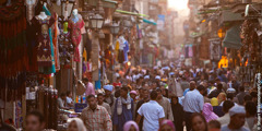 A crowd of people in the Middle East walk on a street lined with shops
