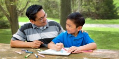 As a little boy draws a picture, his father puts his arm around him