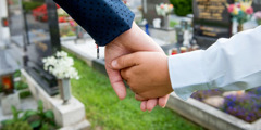 A child holds an adult’s hand in a cemetery