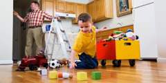 Een jongetje dat zijn speelgoed opruimt terwijl zijn vader een keukenmuur schildert