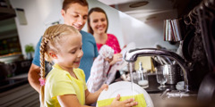 Maža mergaitė plauna indus, jai padeda tėvai
