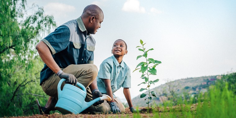 A father helps his son to water a plant