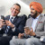 A Caucasian man and a Sikh man sitting next to each other on a plane. They happily converse with each other.