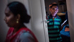 Um menino assustado com o celular na mão, fechando a porta do quarto enquanto a mãe passa por ele.