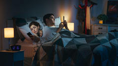 בעל ואישה במיטה מאוחר בלילה כשכל אחד מהם בסמרטפון שלו.‏