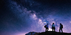 Nogle på vandretur står på toppen af et bjerg og ser på en stjerneklar himmel.