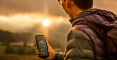 Ein Mann schaut in einer App auf seinem Smartphone nach, wann die Sonne untergeht.