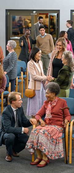 Inside a Kingdom Hall of Jehovah’s Witnesses before a congregation meeting. People of various ages and backgrounds warmly greet and converse with one another.