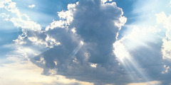 Отворена Библија и сунчева светлост која се пробија кроз облаке