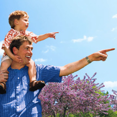 Vater zeigt seinem kleinen Kind, das auf seinen Schultern sitzt, freudestrahlend etwas in der Natur