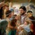 Jesús abrazando tiernamente a niños de distintas edades mientras los padres lo miran.