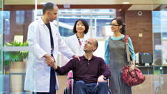 El paciente y su esposa salen del hospital. El médico le da la mano al paciente.