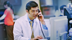 A doctor talking on the phone while he uses a computer.