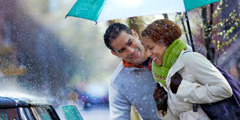 Ein Ehemann hält einen Regenschirm und öffnet seiner Frau die Autotür, damit sie beim Einsteigen nicht nass wird