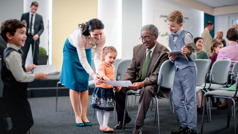 Een ouderling praat in de Koninkrijkszaal met kleine kinderen en bekijkt hun tekeningen