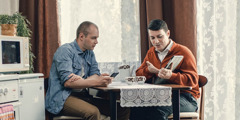 Свидетел на Йехова изучава Библията с мъж в дома му, като и двамата използват електронни устройства, за да четат от Библията и от материала за изучаване, основан на нея