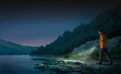 رجل يمشي في المساء على طريق مليء بالصخور قرب بحيرة ويحمل مصباحا ليضيء الطريق