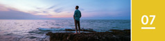 7 урок. Мъж стои на скалист бряг и гледа океана на здрачаване.