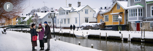 F. Twee van Jehovah se Getuies preek vir ’n vrou op ’n sypaadjie vol sneeu langs ’n kanaal in Swede.