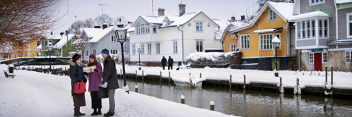 F. Dvojice svědků Jehovových si povídá se ženou na zasněženém chodníku, který vede podél vodního kanálu ve Švédsku