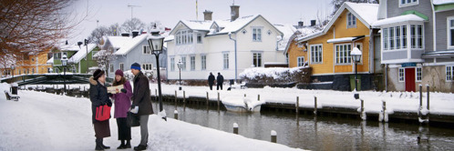 F. Auf einer verschneiten Straße an einem Kanal in Schweden predigen zwei Zeugen Jehovas einer Frau.