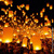 Hundreds of people releasing illuminated lanterns into the night sky during a festival.