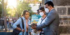 A Witness couple wearing face masks and showing a scripture to a young woman while doing cart witnessing.
