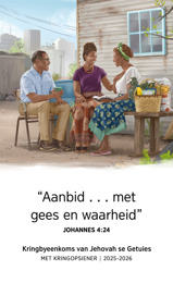 ’n Suster wat in ’n beskeie huis in ’n groot stad woon, glimlag terwyl sy aanmoediging uit die Bybel kry by ’n Getuie-paartjie wat vir haar ’n bietjie kos en ander voorraad gebring het.
