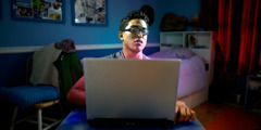 Młody mężczyzna siedzi sam w ciemnym pokoju i ogląda na ekranie komputera kuszące obrazy