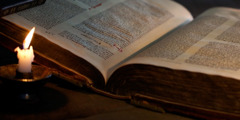Otevřená Bible ve světle svíčky