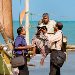 2人のエホバの証人が浜辺で伝道活動を行ない，1人の男性に聖書を見せている