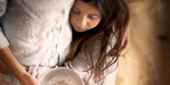 A woman holds an empty bowl and embraces a little girl