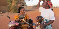 While on her three-wheeled motor scooter, Sarah Maiga preaches to a woman and a little girl