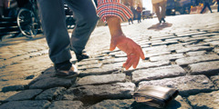 A man reaches for a wallet that is lying on the street