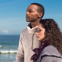 A grieving couple on the beach hold each other and look into the distance