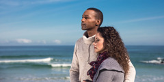 Um casal de luto na praia abraçado olha para o horizonte