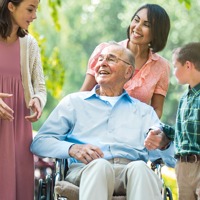 A sick man in a wheelchair is surrounded by loved ones