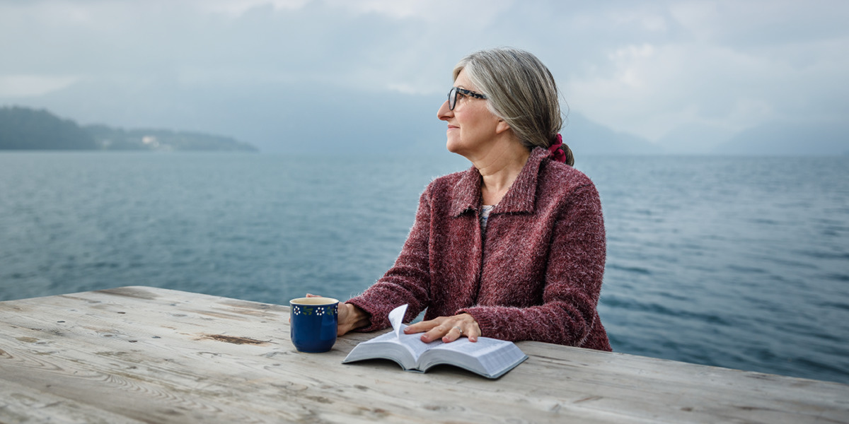 Una mujer sentada mirando al horizonte con una Biblia abierta sobre la mesa