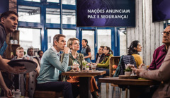 Clientes de uma cafeteria se impressionam com a notícia “Nações anunciam paz e segurança!”, mas o casal de Testemunhas de Jeová não é enganado