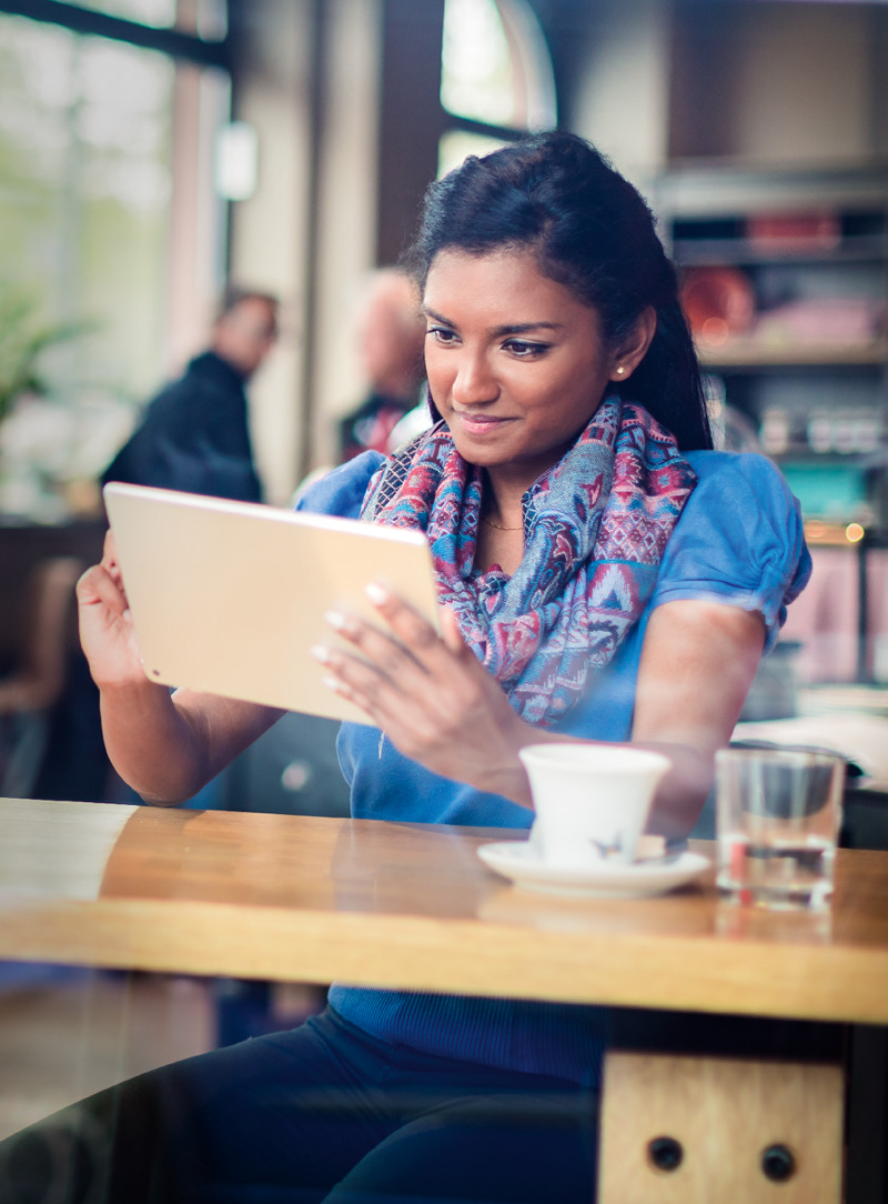 Una joven en una cafetería leyendo la Biblia en su dispositivo electrónico