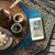 Еден мобилен телефон стои на маса покрај две шолји со кафе. На екранот е прикажана брошурата „Real Faith—Your Key to a Happy Life“.