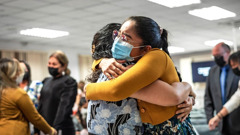 Two sisters happily embracing each other at a Kingdom Hall. All attendees are wearing face masks.